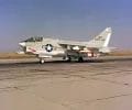 A left front ground view of an A-7C Corsair II aircraft with a Skipper Laser-Guided Bomb (LGB) mounted under its wing.